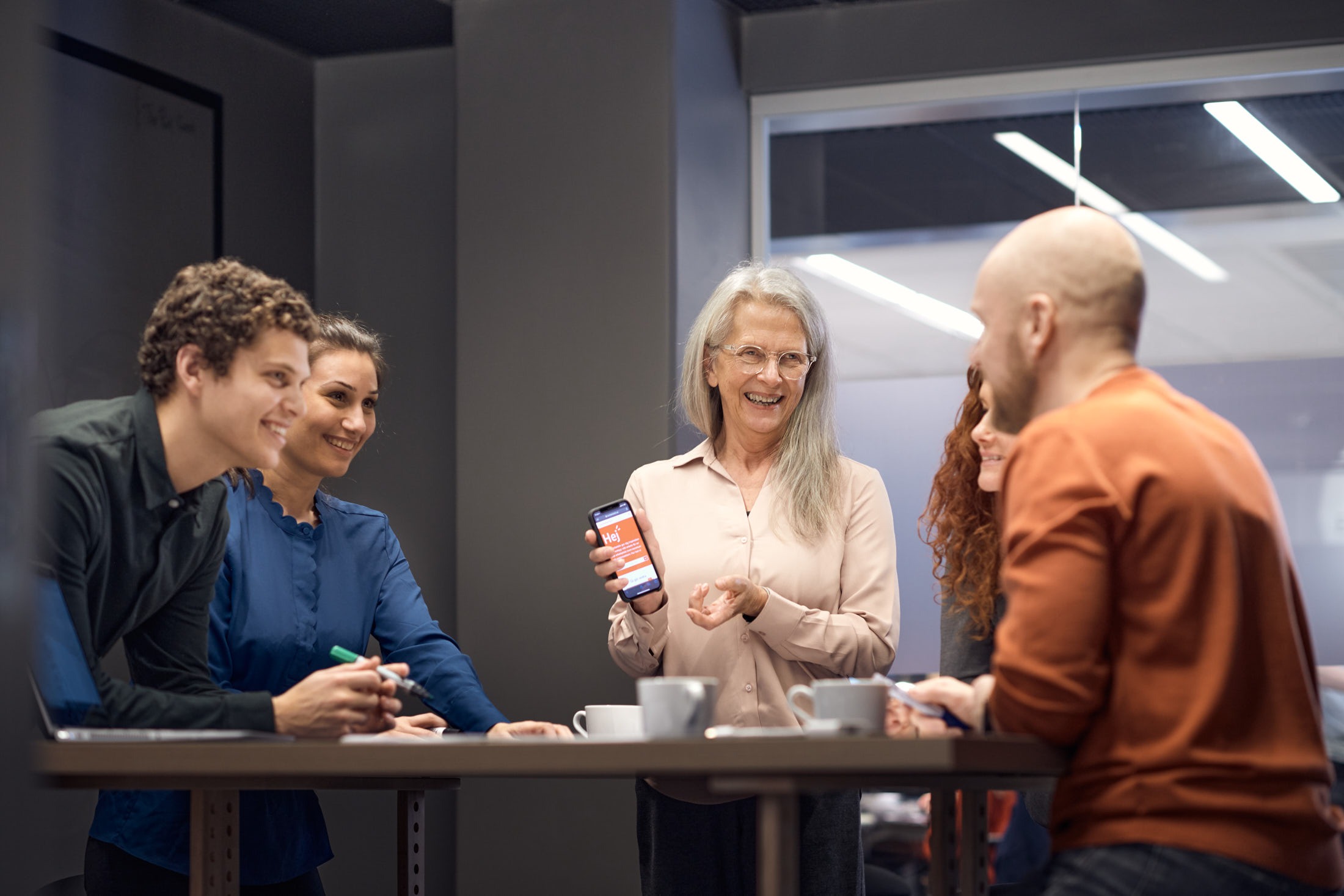 Fyra personer st&aring;r runt ett konferensbord och samtalar