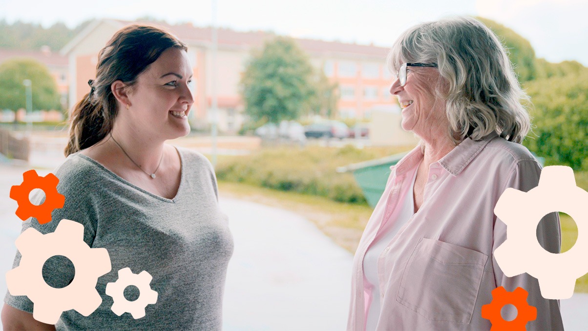 Tv&aring; kvinnor st&aring;r utomhus, tittar mot varandra och ler
