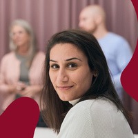 kvinna som vänder sig om och ser in i kameran. Bakom henne syns en arbetsgrupp som pratar med varandra.