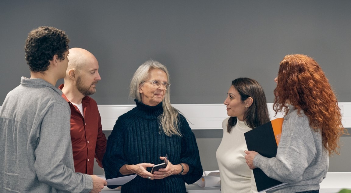Fem personer st&aring;r i grupp och samtalar.