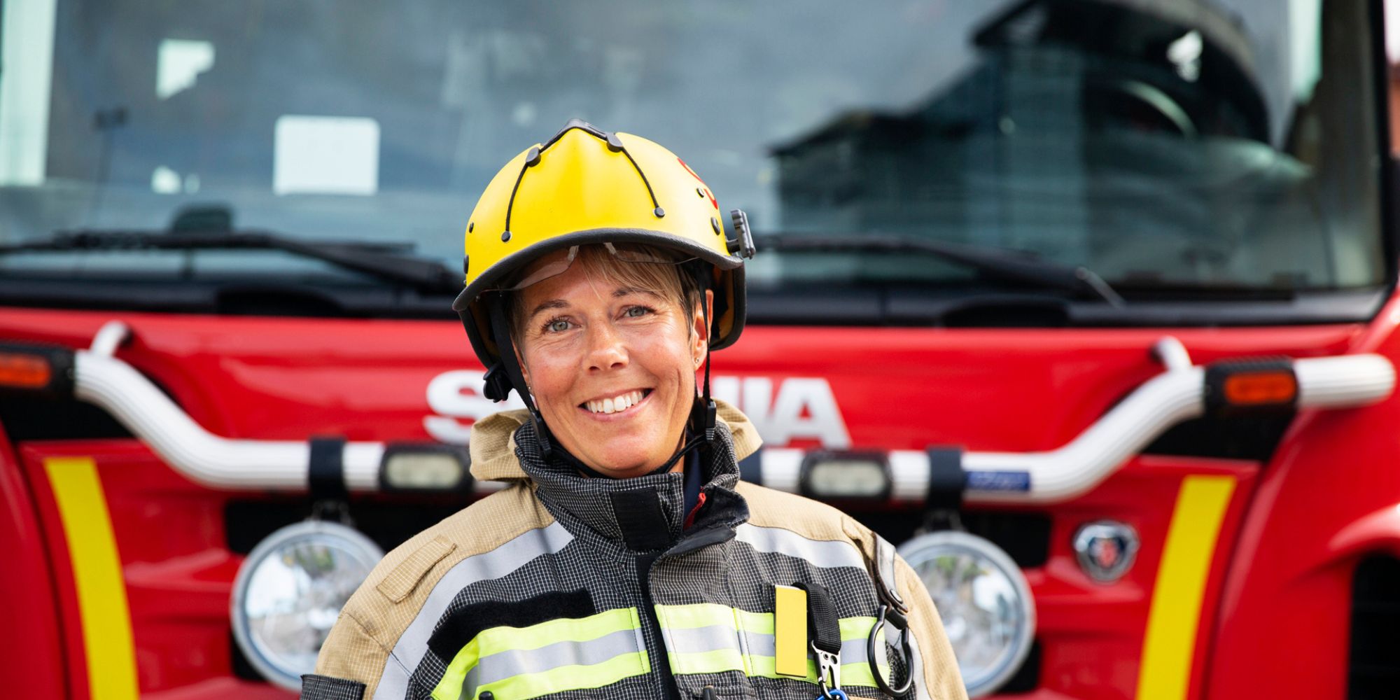 Kvinnlig brandman som ler och st&aring;r framf&ouml;r en brandbil.