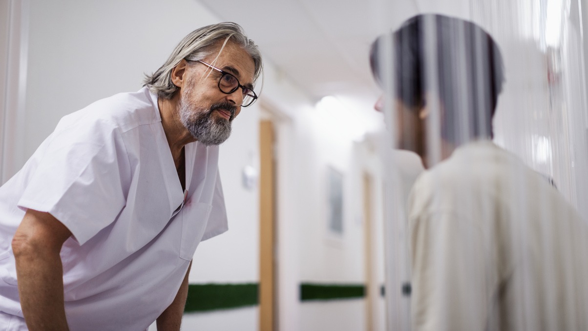 Sjukv&aring;rdare lutar sig fram emot en patient. Patienten sitter i en korridor.
