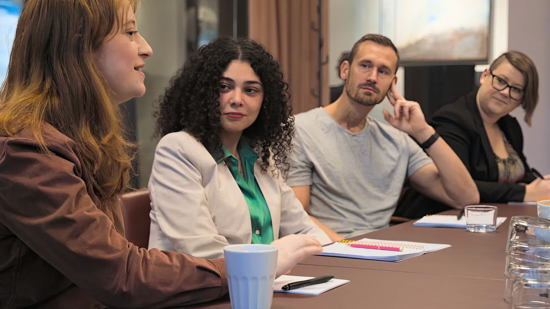 Fyra kollegor i m&ouml;te vid ett konferensbord. En kvinna pratar och tre kollegor lyssnar och anteckningar.