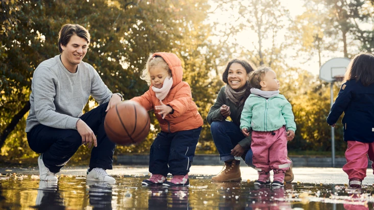 Tv&aring; f&ouml;rskolebarn leker med basketboll i vattenp&ouml;l med tv&aring; pedagoger bredvid