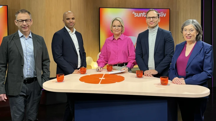 en grupp m&auml;nniskor st&aring;r bakom ett stort bord i en studio.