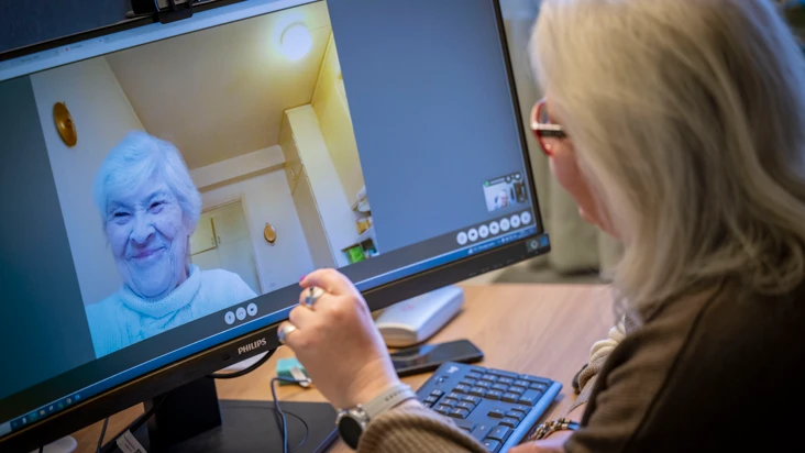 En kvinna fr&aring;n hemtj&auml;nsten sitter framf&ouml;r en datorsk&auml;rm och pratar med en brukare.