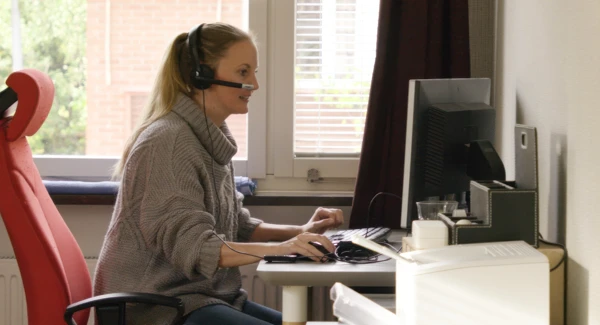 En kvinna sitter vid ett skrivbord och anv&auml;nder en dator.