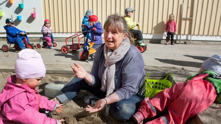En kvinna sitter i en sandl&aring;da med en grupp f&ouml;rskolebarn.