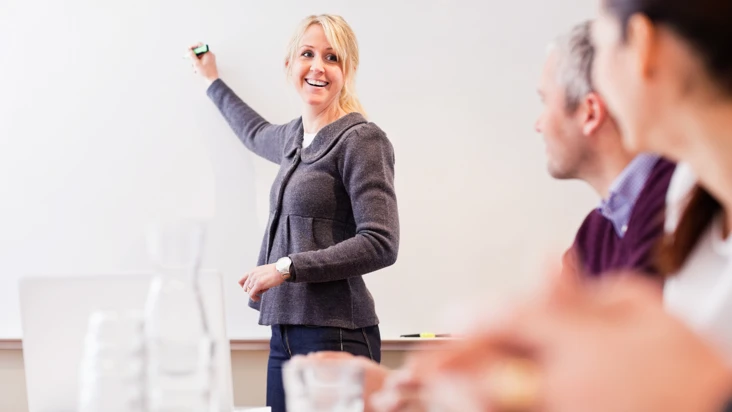Kvinna f&ouml;rklarar och skriver p&aring; en whiteboard f&ouml;r kollegor.
