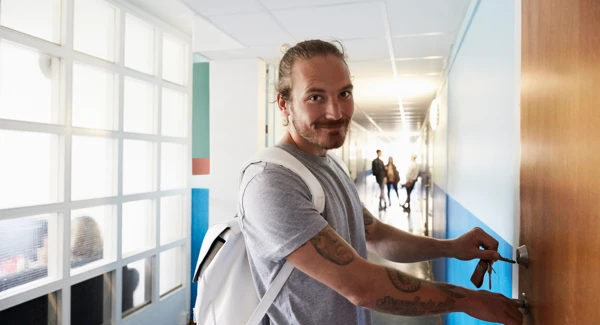 En man st&aring;r i en korridor och l&aring;ser en d&ouml;rr.