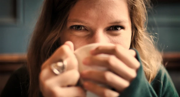 En kvinna h&aring;ller en kaffekopp med tv&aring; h&auml;nder n&auml;ra ansiktet.