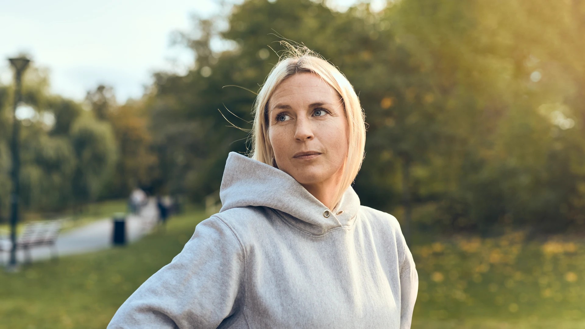 Kvinna i gr&aring; huvtr&ouml;ja st&aring;r p&aring; en gr&auml;smatta.