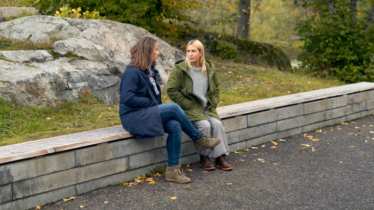 Tv&aring; kvinnor sitter p&aring; toppen av en stenmur och pratar.