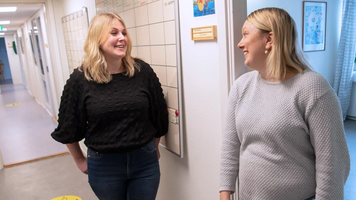 Tv&aring; kvinnor st&aring;r och pratar i en korridor.