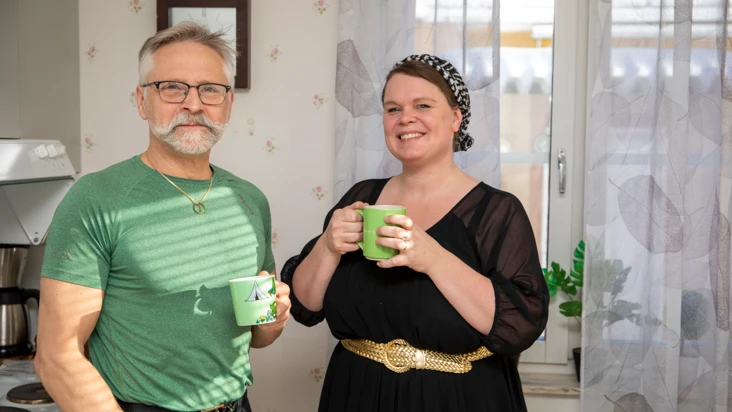 En man och en kvinna st&aring;r med kaffekoppar och tittar mot kameran.