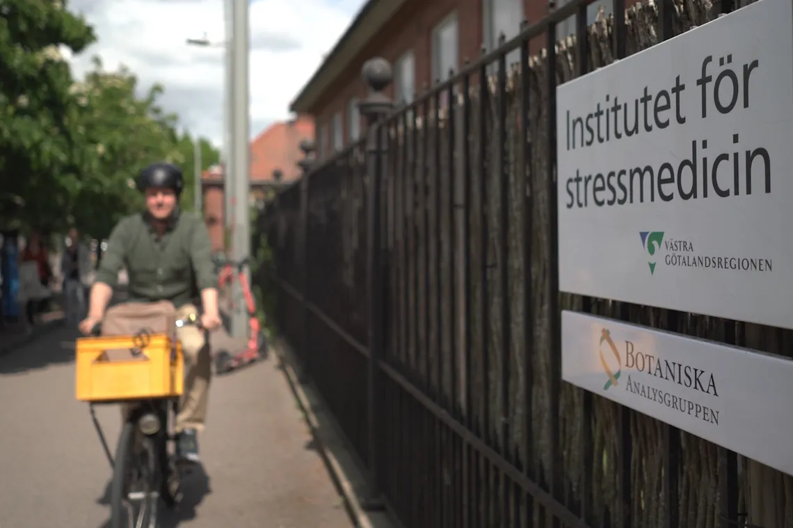 En man som cyklar l&auml;ngs en gata bredvid ett staket.